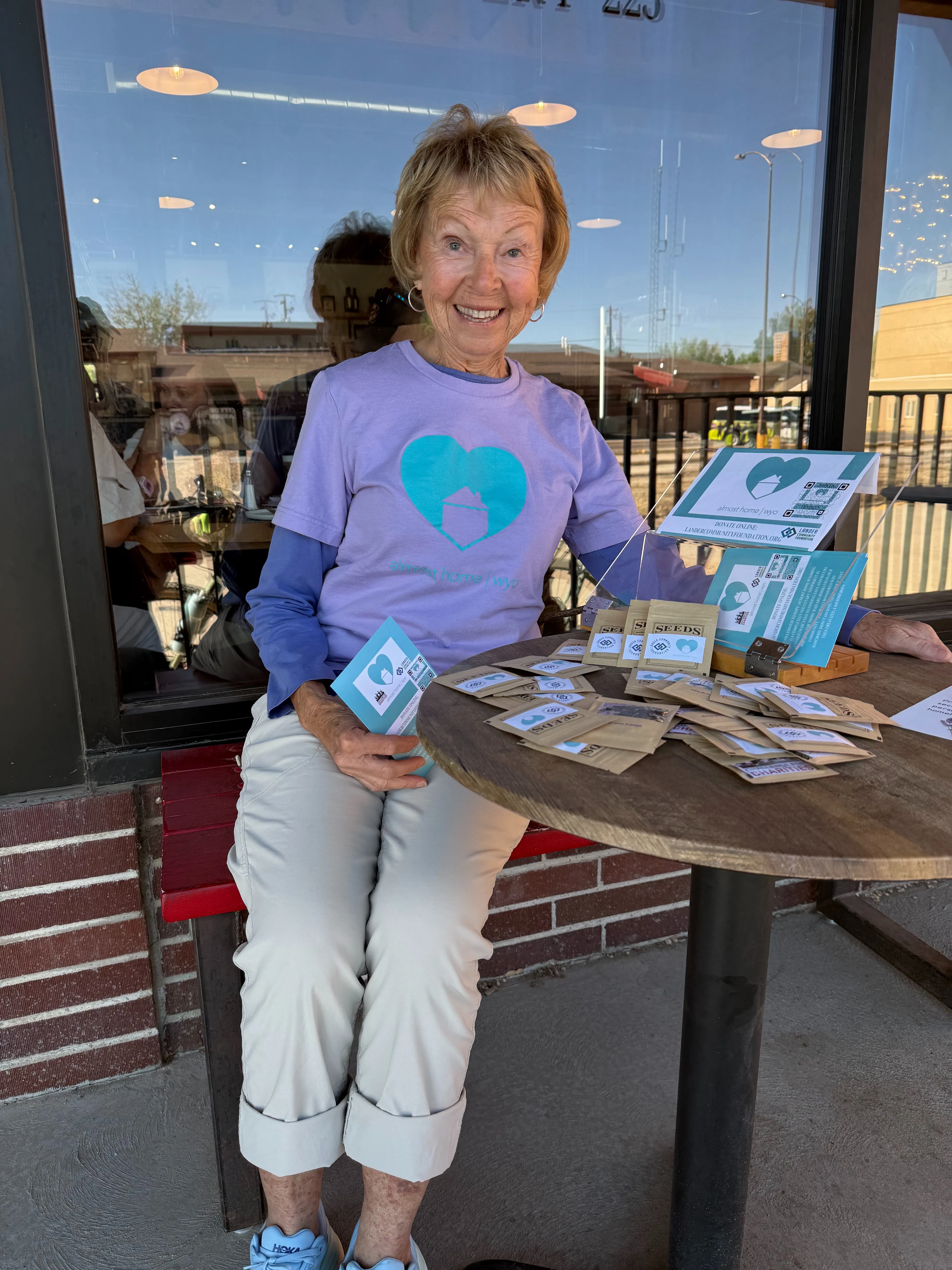Member of Almost Home Wyoming smiling at their booth to give out Seeds at the Lander Bake Shop